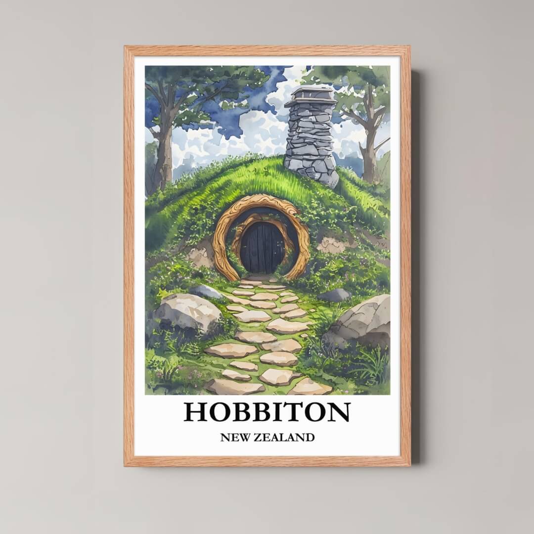 A framed, whimsical illustration of a Hobbit Hole entrance in Hobbiton, New Zealand, with a light wood frame, featuring a lush green landscape.